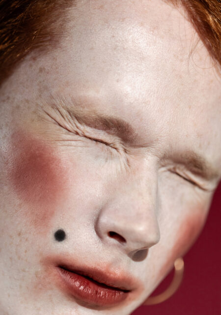 Androgynous man with retro makeup and mole on pale face squinting Androgynous man with retro makeup and mole on pale face squinting